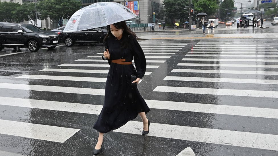 Женщина с зонтиком переходит дорогу в центре Сеула, Южная Корея.