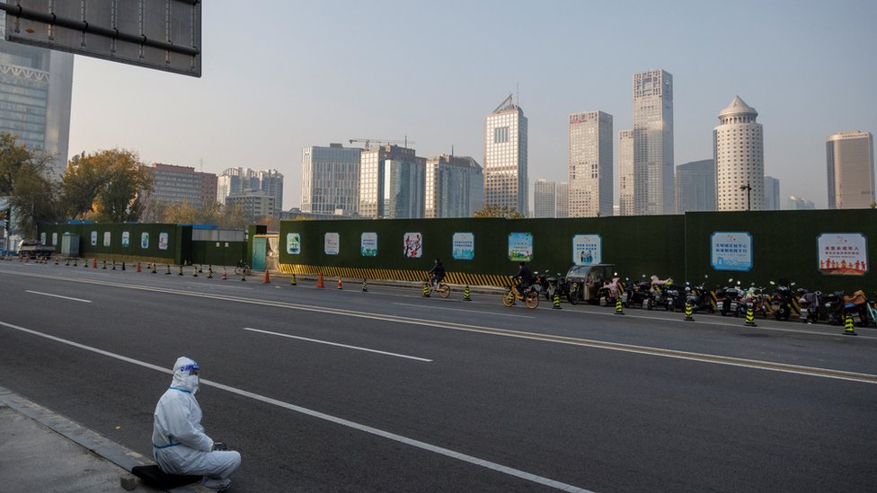 一名身穿防護服的北京防疫工作者坐在中央商務區 (CBD) 的人行道上