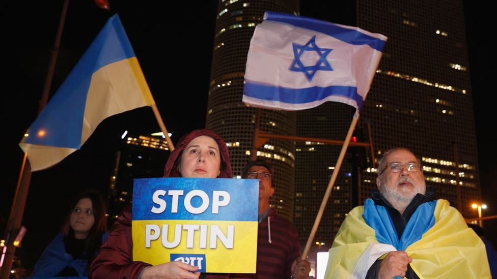 Una mujer con un cartel contra la guerra en Ucrania y un hombre con la bandera de Ucrania en una protesta en Tel Aviv