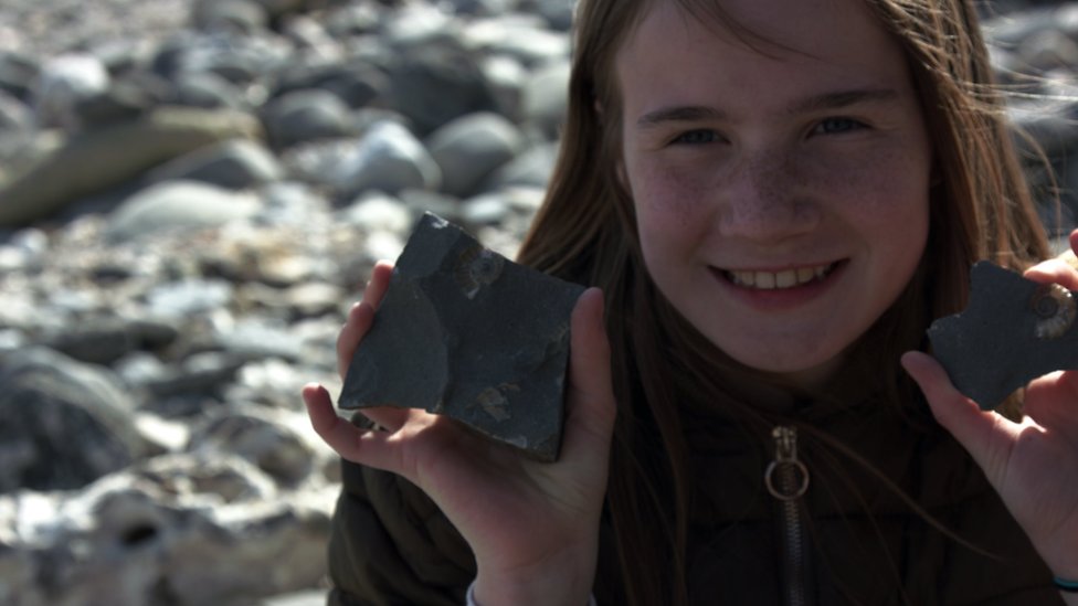 Evie at the beach in Lyme Regis, holding two fossils she's found