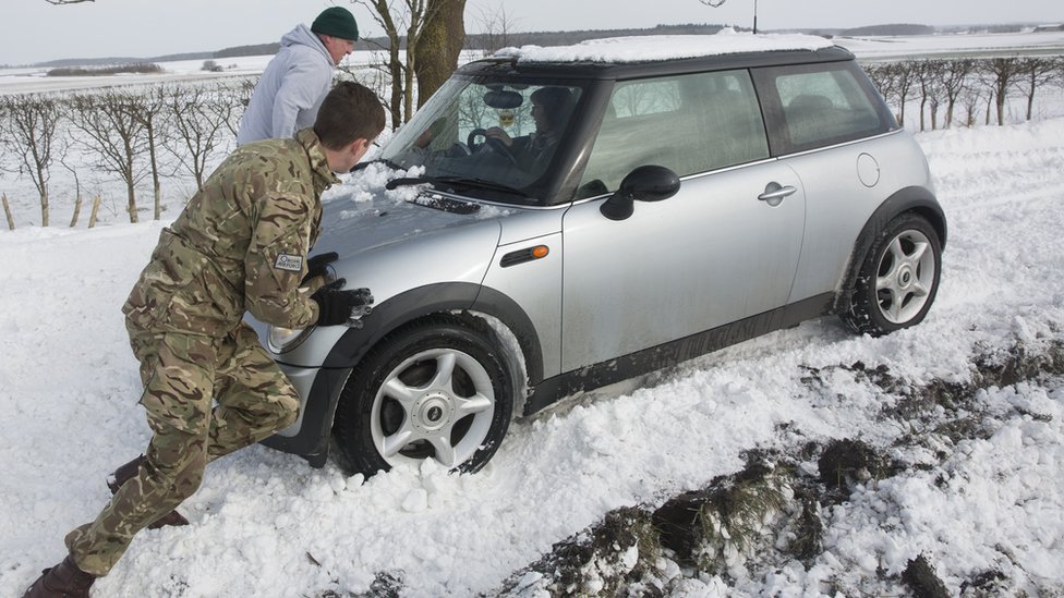 Мужчина выталкивает машину из снега