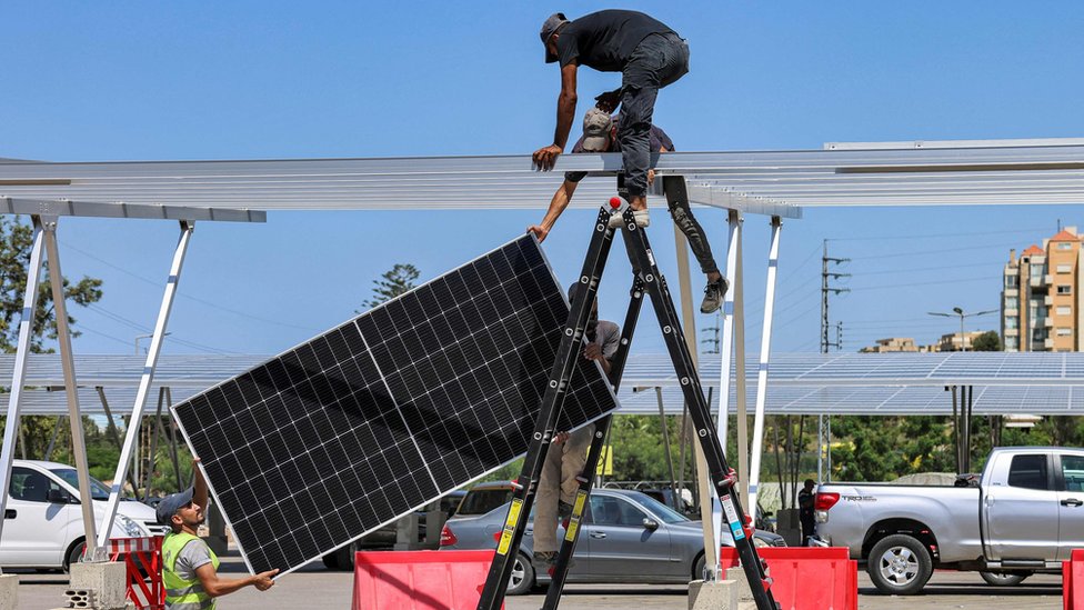 عمال يقومون بتركيب ألواح شمسية جديدة كظلال فوق المركبات في مرآب السيارات بمركز تجاري في مدينة جبيل شمال لبنان في 26 أغسطس 2022
