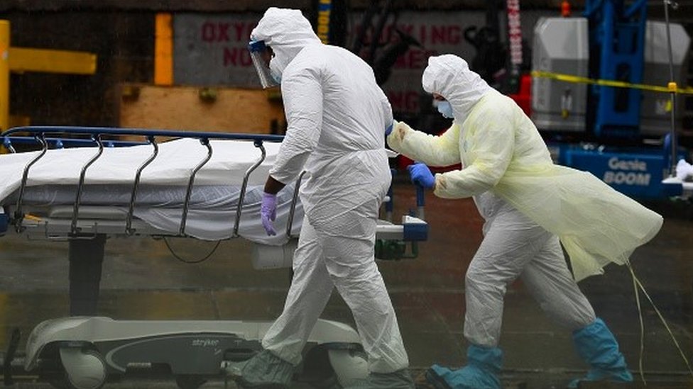 Medical personnel move a deceased patient to a refrigerated truck serving as makeshift morgue