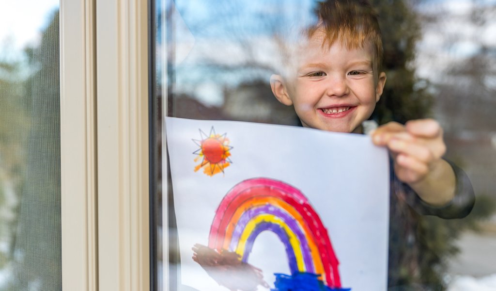 Niño pegando dibujo de arcoíris en la ventana