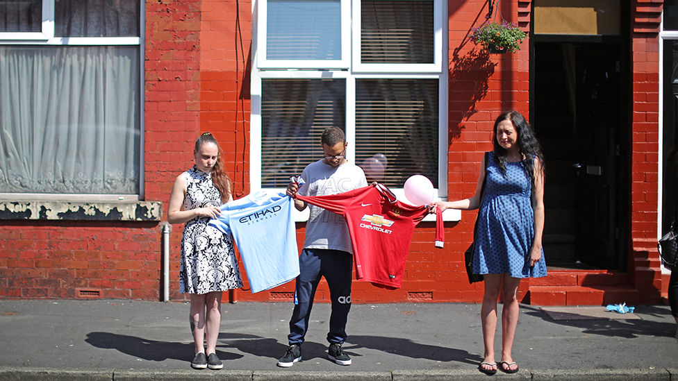 Три человека держат футболку «Манчестер Юнайтед» и футболку «Манчестер Сити»