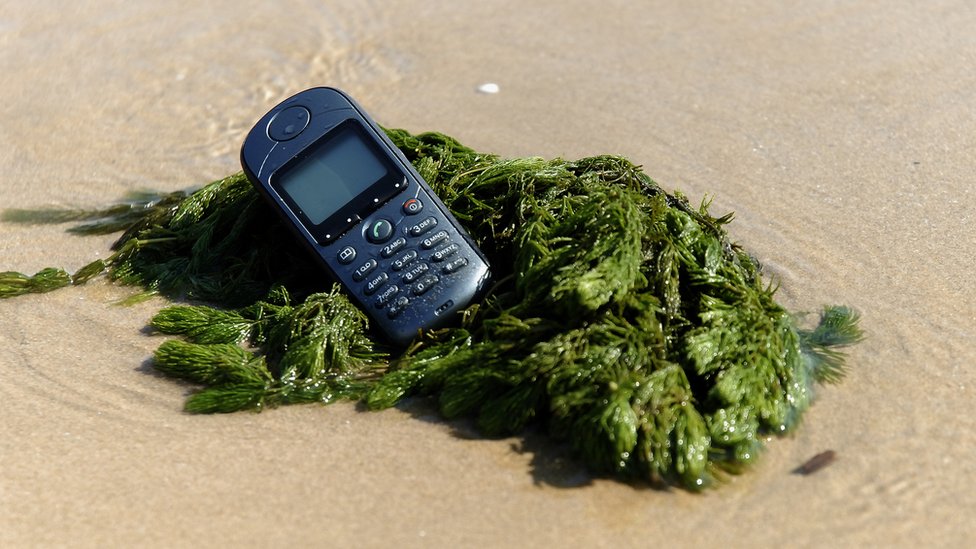 Algunos idiomas serán tragados por la ola de las nuevas tecnologías. teléfono móvil descatalogado en la orilla de la playa.
