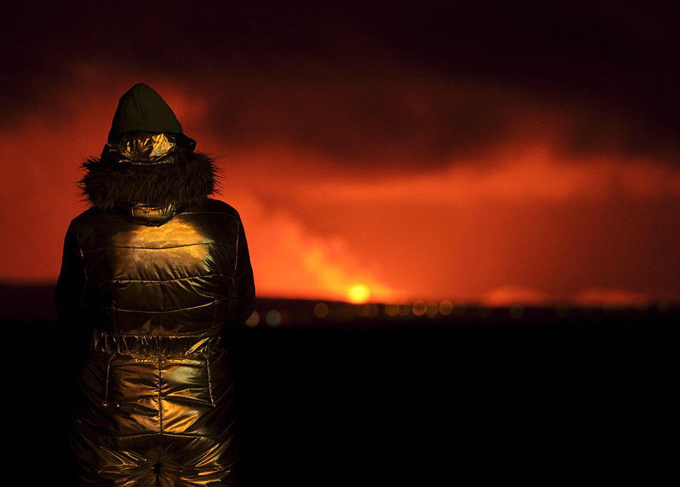 An onlooker stands by the shoreline in Reykjavik to watch the volcanic eruption - 19 December 2023