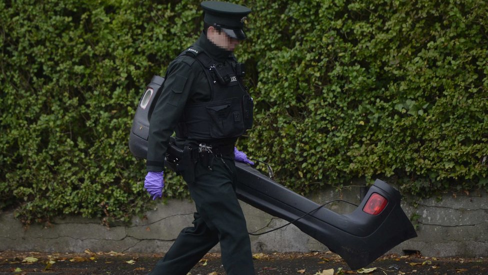 Полицейский снимает бампер с фургона, сбившего Энду Долан с места крушения на Мэлоун-роуд в Белфасте