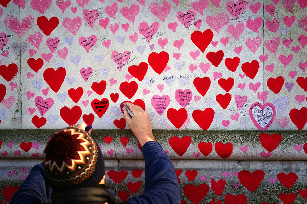 رجل يكتب على قلب على الحائط التذكاري لضحايا كوفيد في لندن.