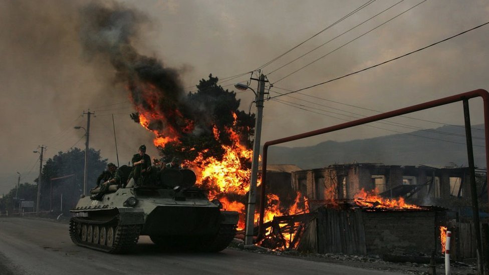 An armored personnel carrier of Russian troops with soldiers on top drives past a house burned down by South Ossetian militias on August 18, 2008 in the Georgian village of Kvemo-Achebeti.