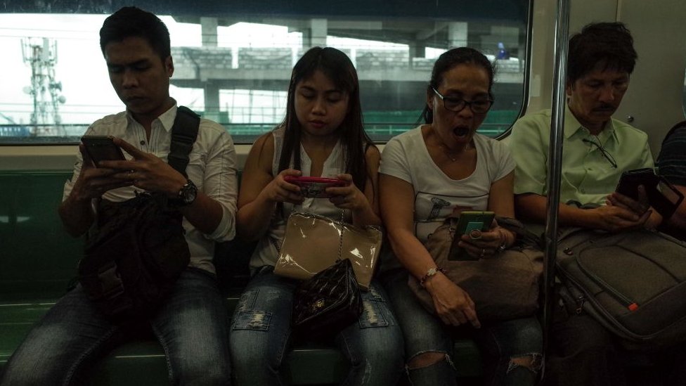 أشخاص تستحوذ عليهم هواتفهم في قطار في مانيلا
