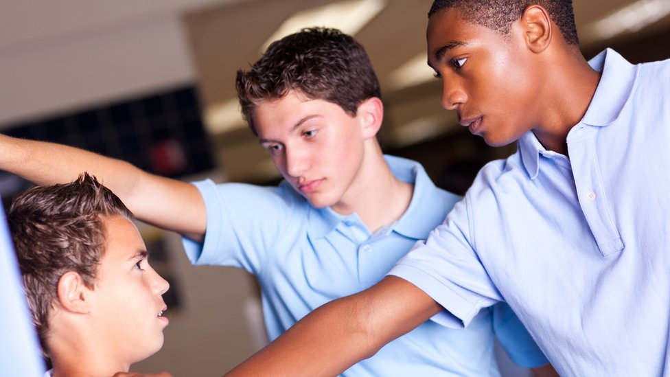 Two boys hold a boy against a wall