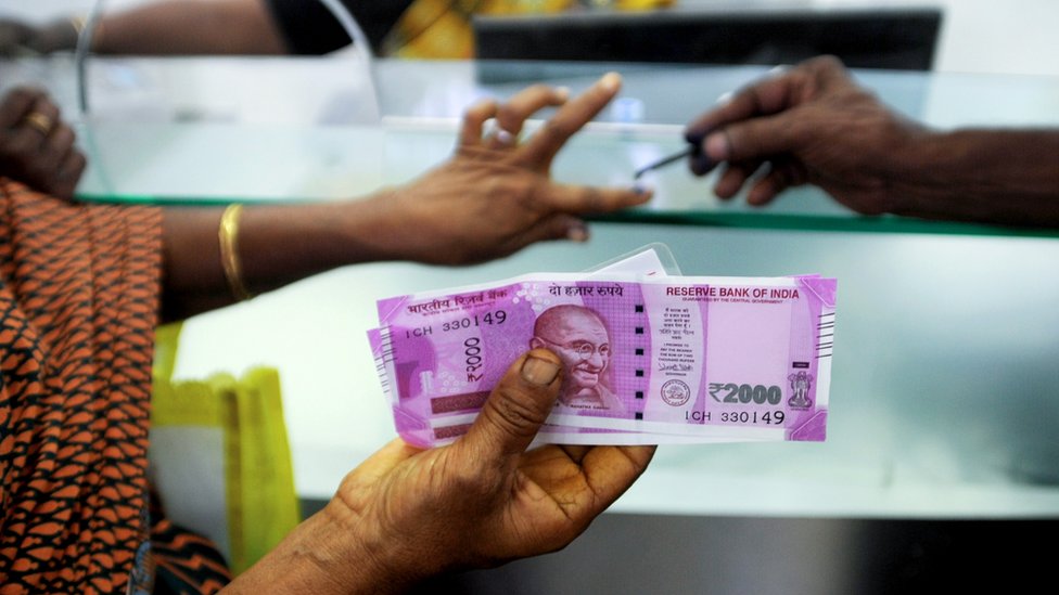 Индийская женщина держит банкноты в 2000 индийских рупий, так как на ее пальце нанесены несмываемые чернила после обмена банкнот в 500 и 1000 индийских рупий в банке в Ченнаи.