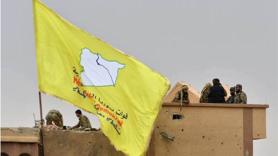 قوات سوريا الديمقراطية ترفع علمها الأصفر على أحد المباني الذي استعادته من تنظيم الدولة الإسلامية في مارس/ آذار الماضي.
