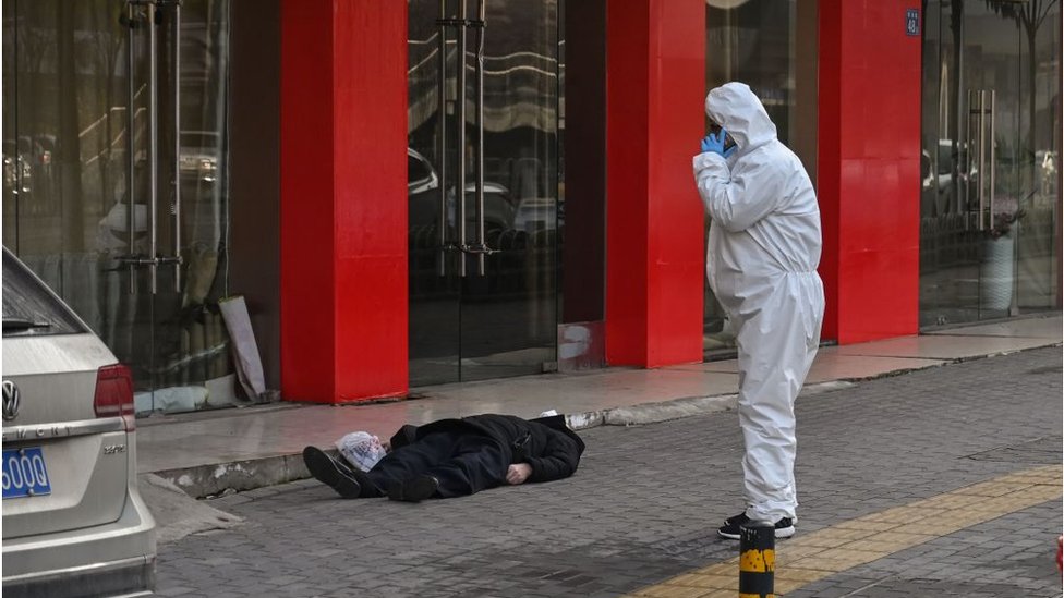 This photo taken on January 30, 2020 shows an official in a protective suit checking on an elderly man wearing a facemask who collapsed and died on a street near a hospital in Wuhan