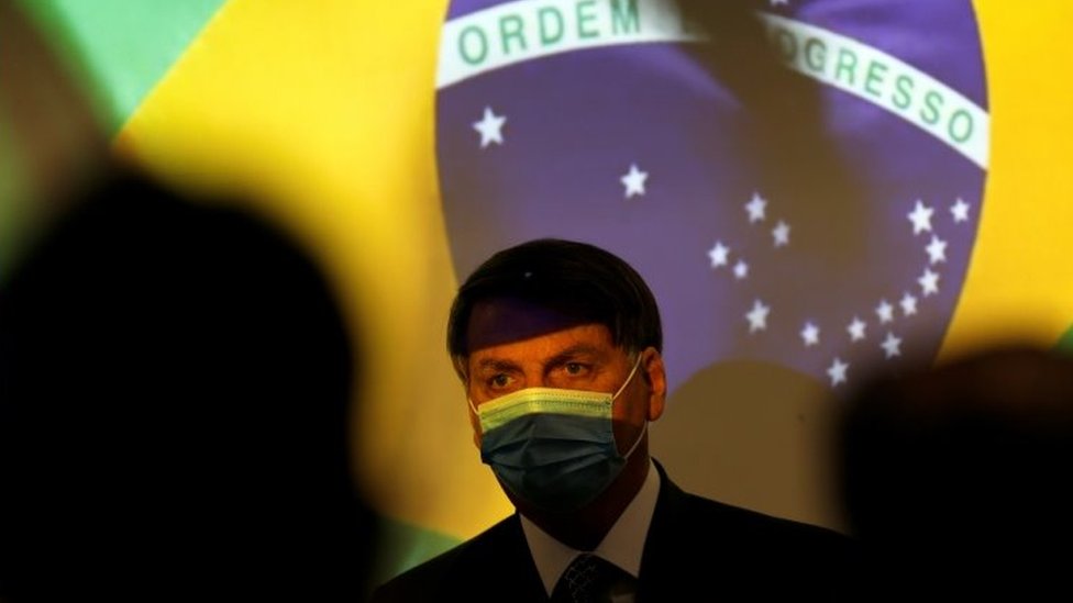 Jair Bolsonaro com a bandeira do Brasil ao fundo