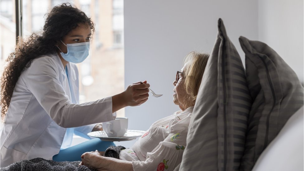 Mujer alimenta a una anciana.