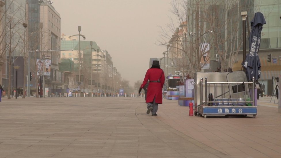 一名身穿紅色外套的保安走過北京一條空無一人的購物街。