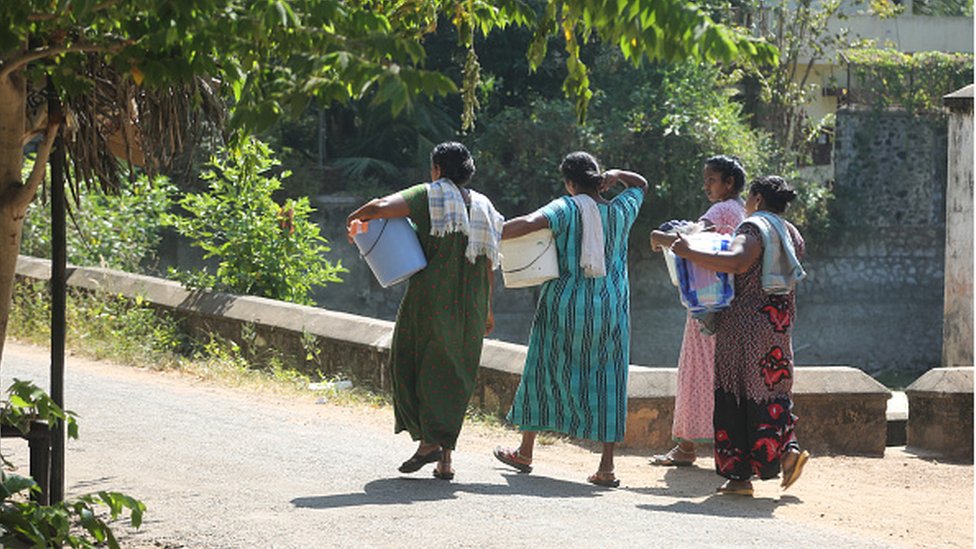 Mujeres indias caminan hacia un río con ropa para lavar.