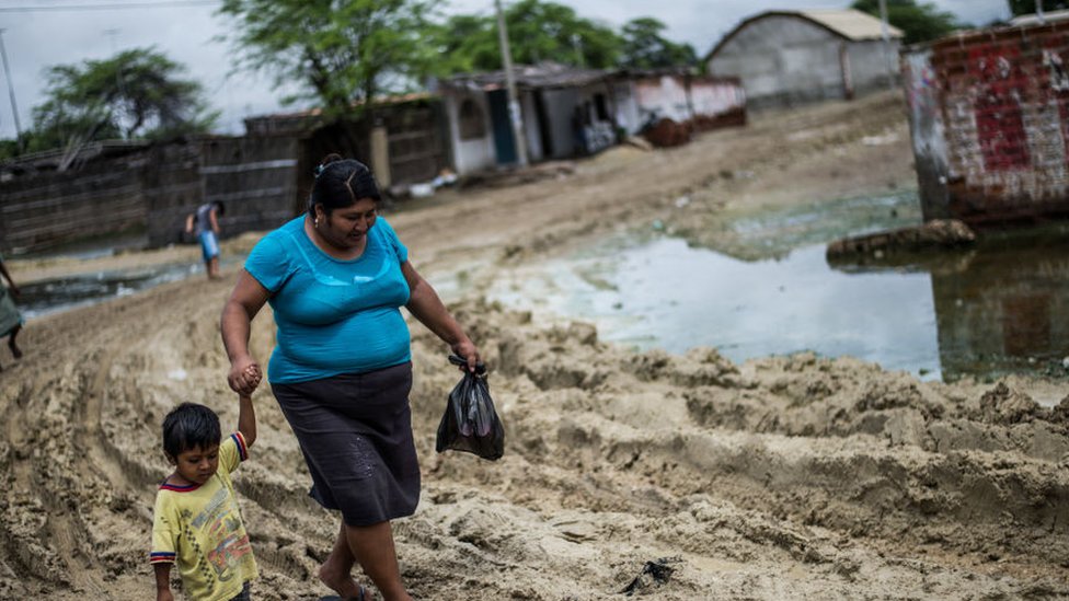 Una mujer con su hijo camina en Piura, después de las inundaciones de 2017.