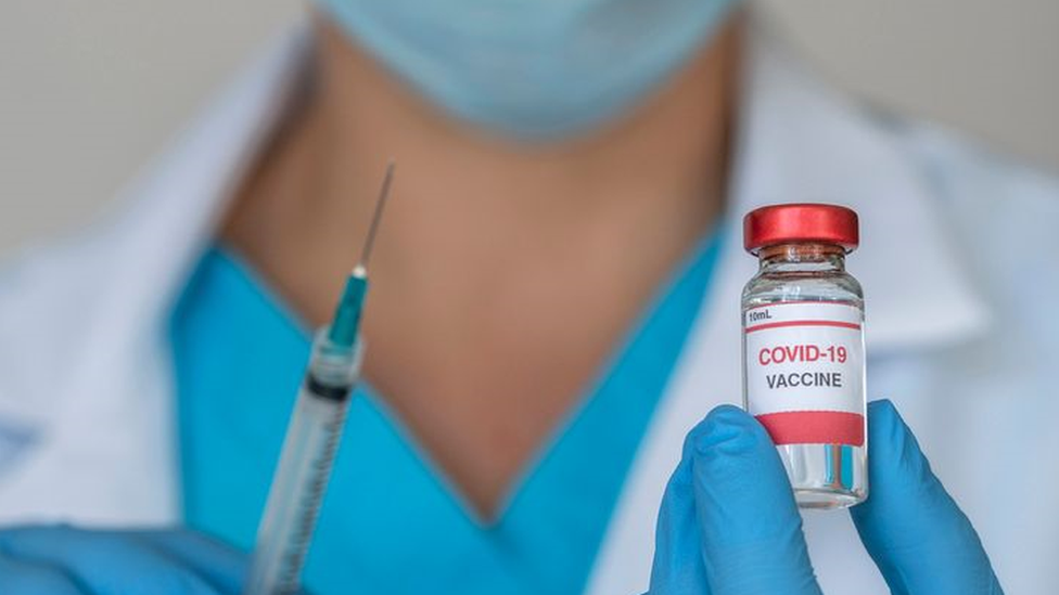 Profissional de jaleco segura seringa e frasco de vidro escrito 'Covid-19 vaccine'
