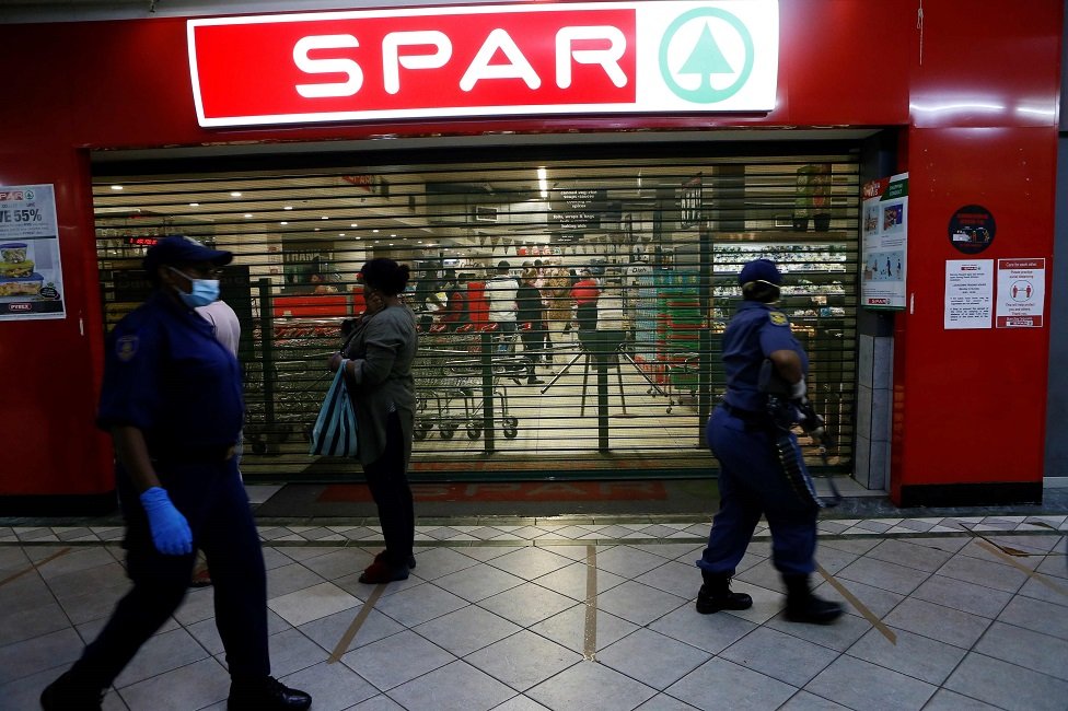 Полицейская служба Южной Африки (SAPS) проходит мимо покупателей, стоящих в очереди у продуктового магазина во время их операции в Саннисайде, Претория, 7 апреля 2020 г.