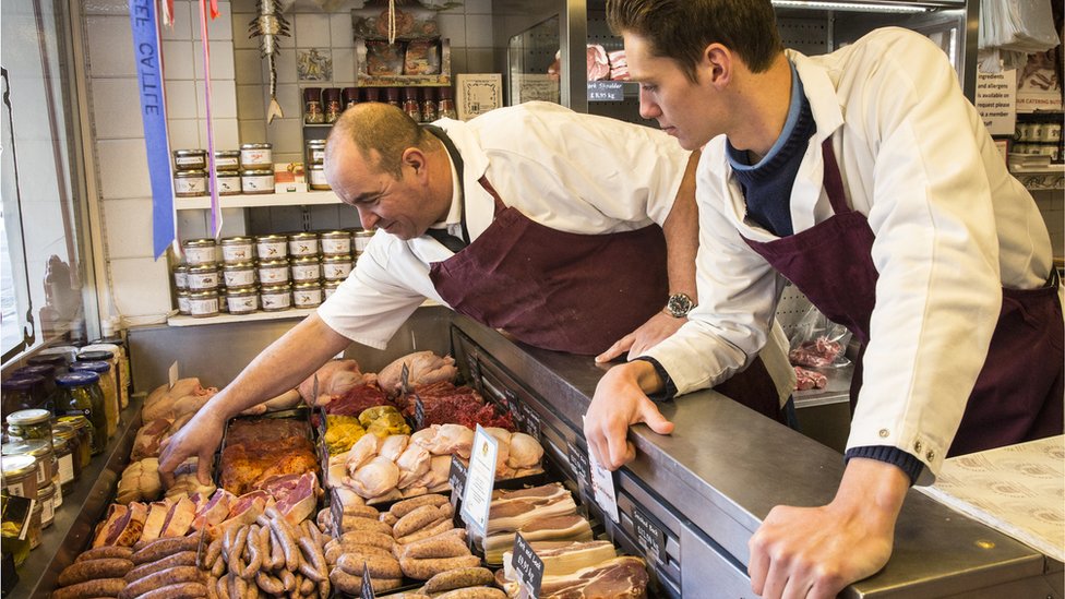 Butchers stand at a counter with raw sausages and other meats