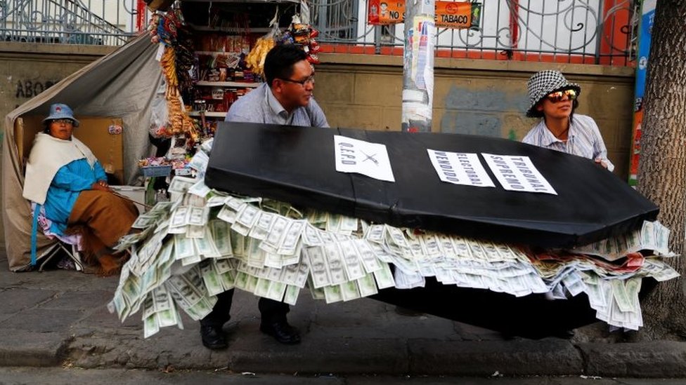 Два человека несут гроб из папье-маше, наполненный бумажными купюрами в Ла-Пасе