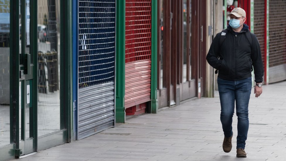 Мужчина в маске проходит мимо закрытых ставнями магазинов в Кардиффе