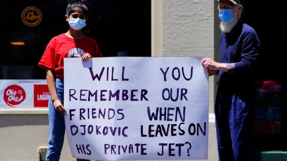 Refugee activists hold a sign reading: 'Will you remember our friends when Djokovic flies out on his private jet'