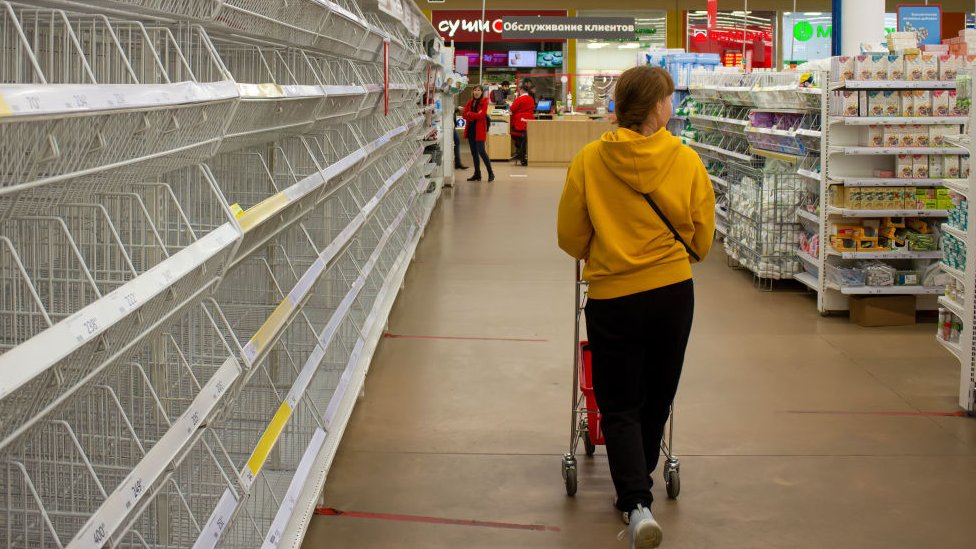 A woman walks by empty shelves in a supermarket in Moscow. There has been shortages of women's sanitary pads, diapers, and sugar