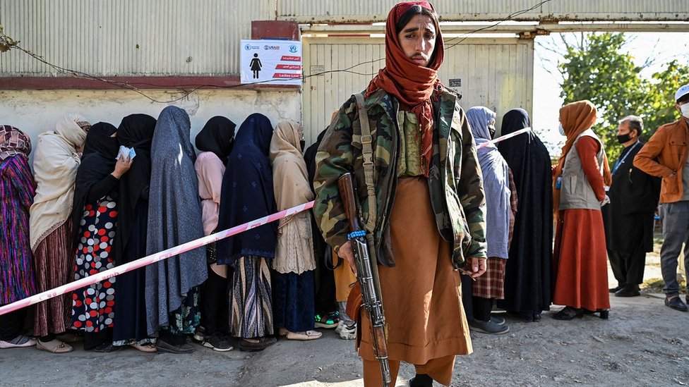 A Taliban fighter stands guard as women wait in line during a World Food Programme food distribution in Kabul