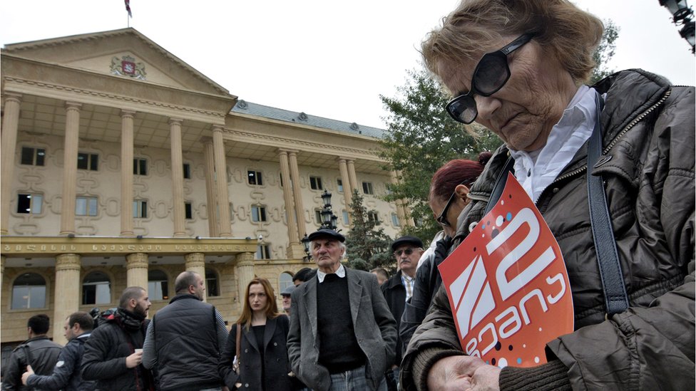 Женщина держит плакат с логотипом телеканала «Рустави 2» во время митинга протеста перед зданием Тбилисского городского суда 22 октября 2015 года.
