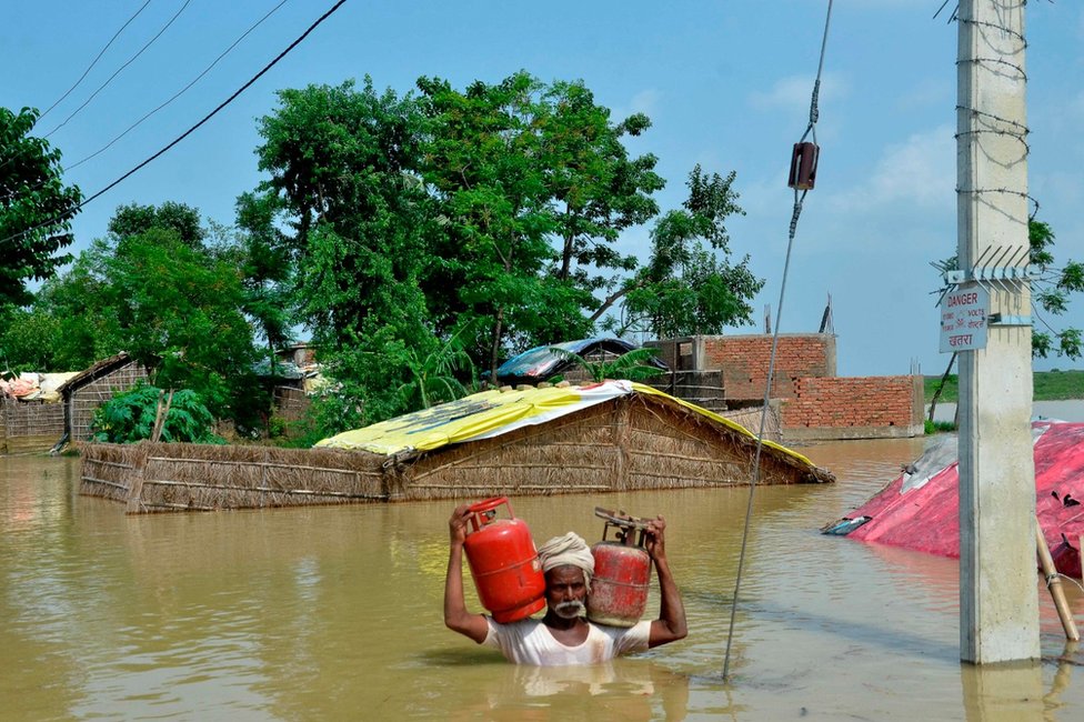Житель Индии несет канистры с газом, пробираясь через затопленный район после сильных муссонных дождей в Музаффарпуре в индийском штате Бихар.