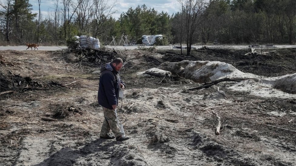 A dosimetrist measures the level of radiation around trenches dug by the Russian military in an area with high levels of radiation, called the Red Forest