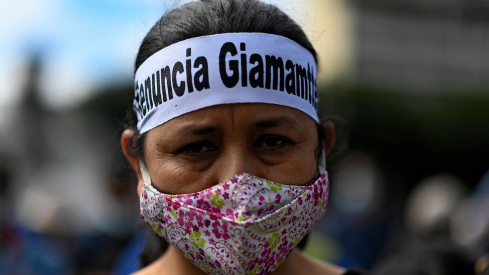 Una manifestante con un pañuelo en la frente que lee "renuncia Giammattei"