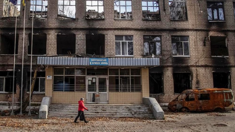 Un hombre camina frente a un edificio escolar bombardeado.