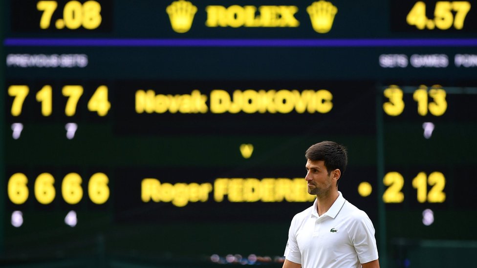 Novak Djokovic in front of the scoreboard showing his winning score over Roger Federer