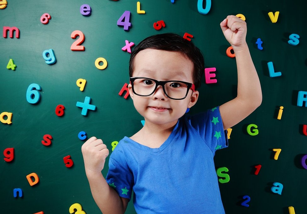 Cute little boy in front of a dark green chalkboard, with colourful magnetic numbers stuck on it
