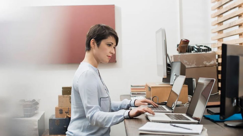 Una mujer trabajo frente a dos computadoras.