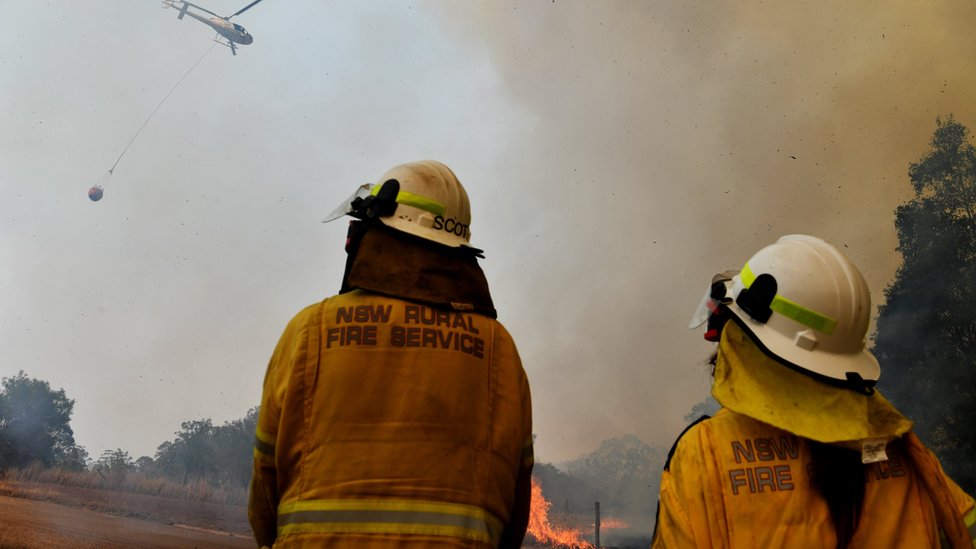Пожарные наблюдают, как вертолет обследует очаг пожара в районе Хиллсайд, Новый Южный Уэльс, 13 ноября