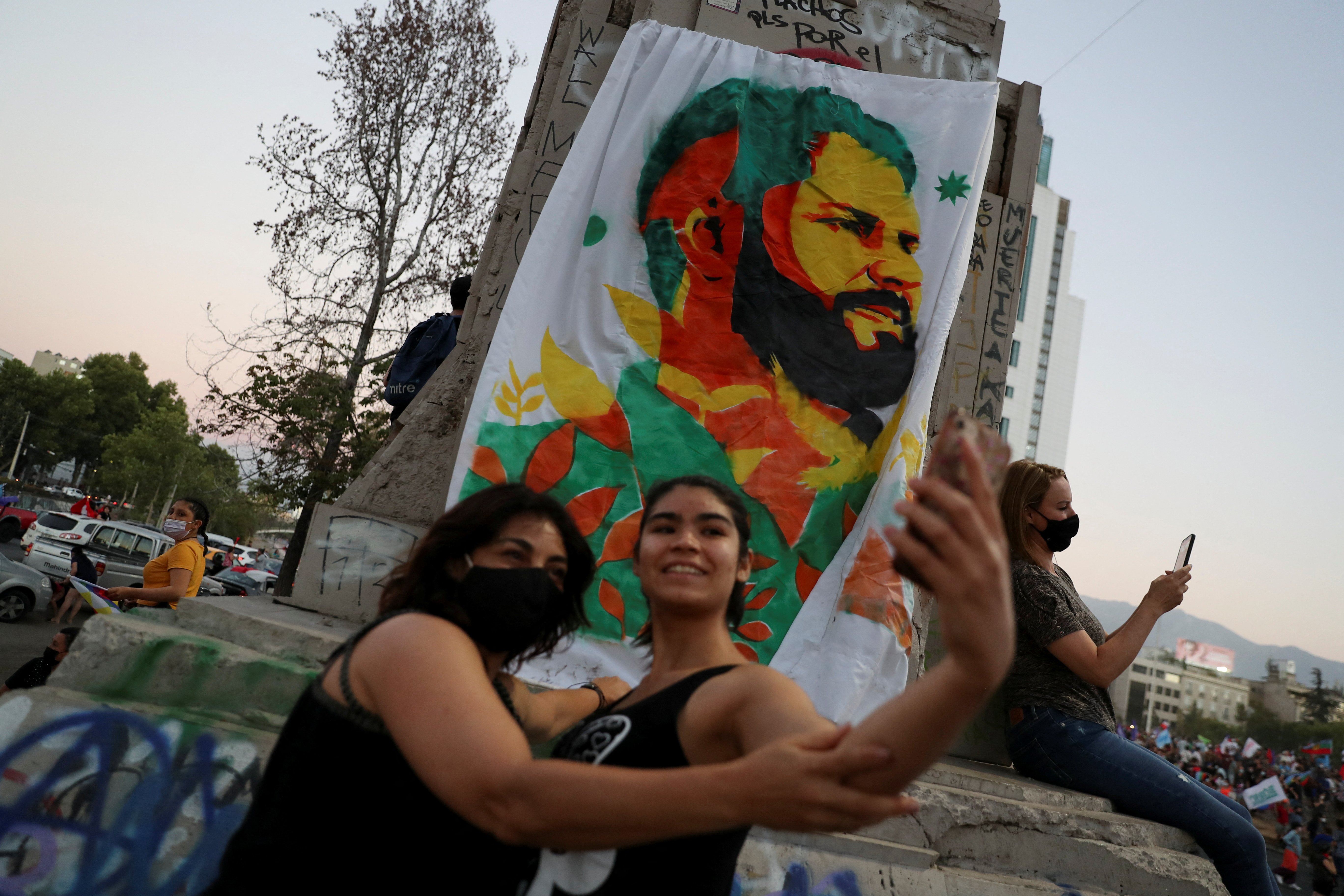 Dos mujeres se toman una foto frente a una pancarta con el rostro de Gabriel Boric