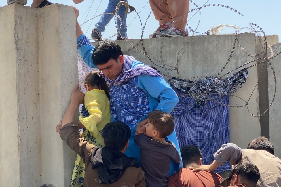People struggle to cross the boundary wall of Hamid Karzai International Airport to flee Afghanistan on 16 August 2021