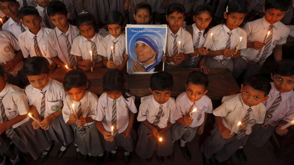 Школьники принимают участие в молитвенной церемонии при свечах, держа портрет Матери Терезы по случаю празднования ее 101-й годовщины в Калькутте, Индия