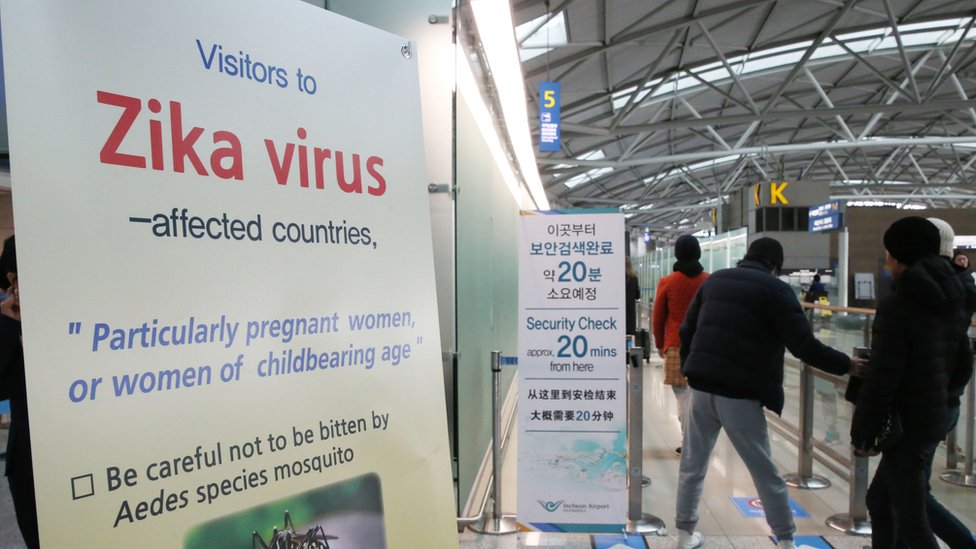 Пассажиры проходят мимо вывески о вирусе Зика в пассажирском терминале международного аэропорта Инчхон в Инчхоне, Южная Корея, во вторник, 22 марта 2016 г.