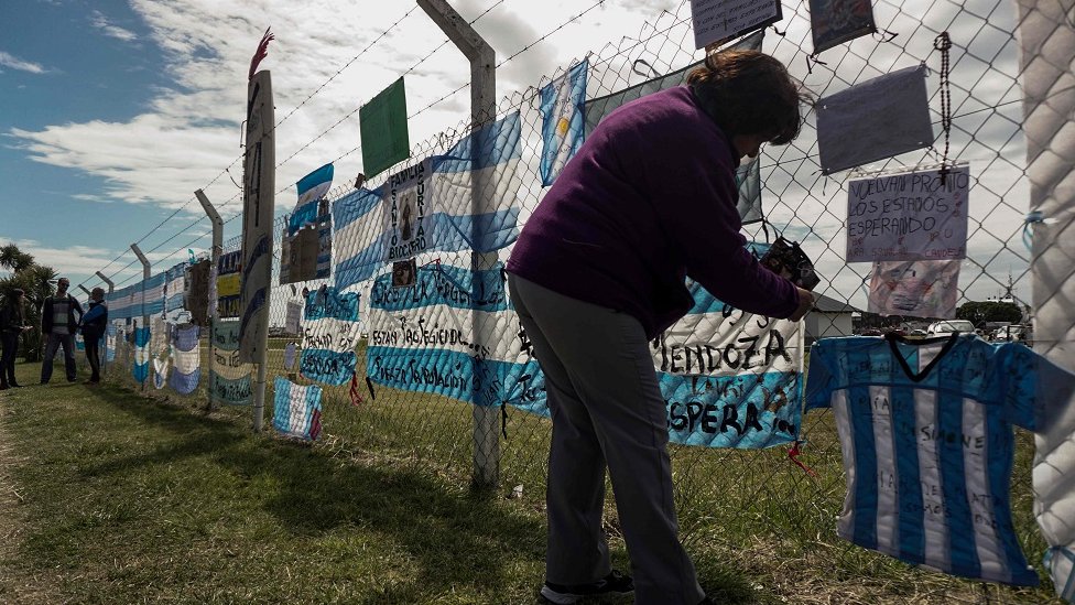 Женщина вешает послание поддержки на аргентинском флаге на заборе