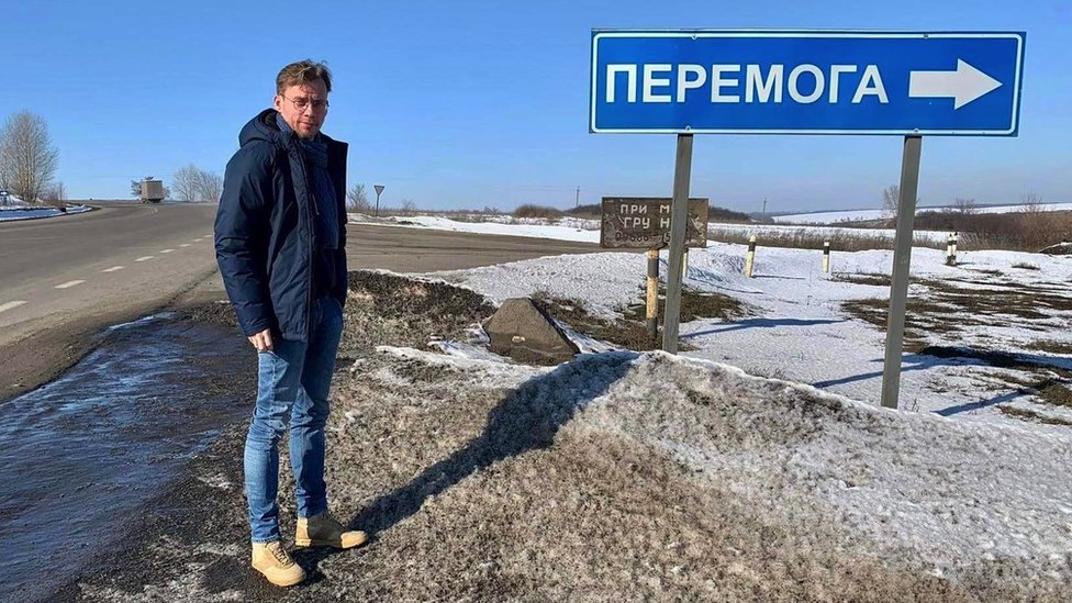 Ilya Barabanov next to a Ukrainian road sign to the town of Peremoha