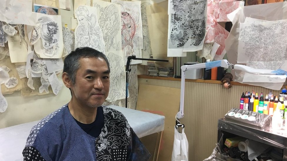 Tattoo artist Horimitsu sitting in his studio in Tokyo, where the walls are lined with tattoo sketches