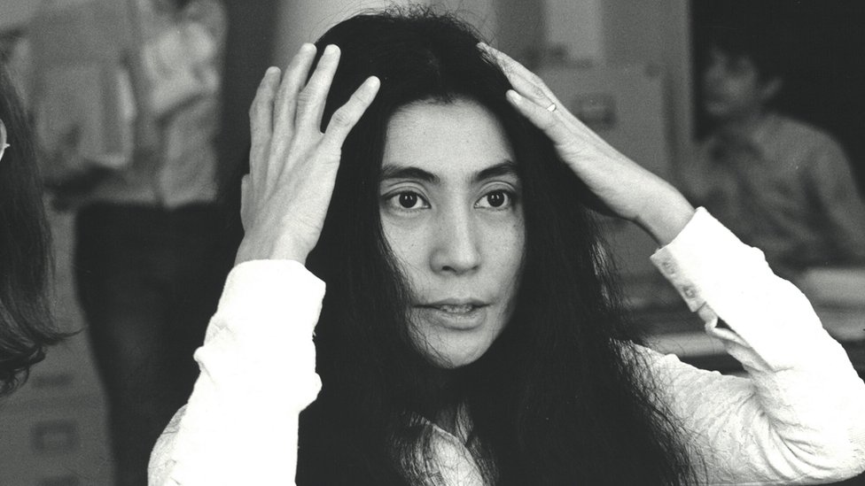 Fotografia em preto e branco mostra Yoko Ono com as mãos no cabelo