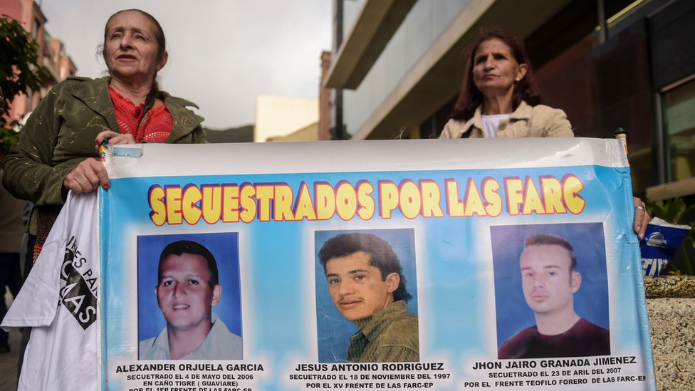 Женщины держат плакат с портретами трех мужчин, похищенных партизанами FARC, во время акции протеста у здания штаб-квартиры особой юрисдикции по вопросам мира (JEP) в Боготе 13 июля 2018 г.